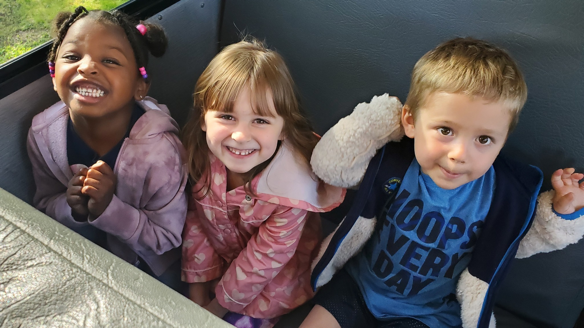 Three preschool students sit in a bus seat together