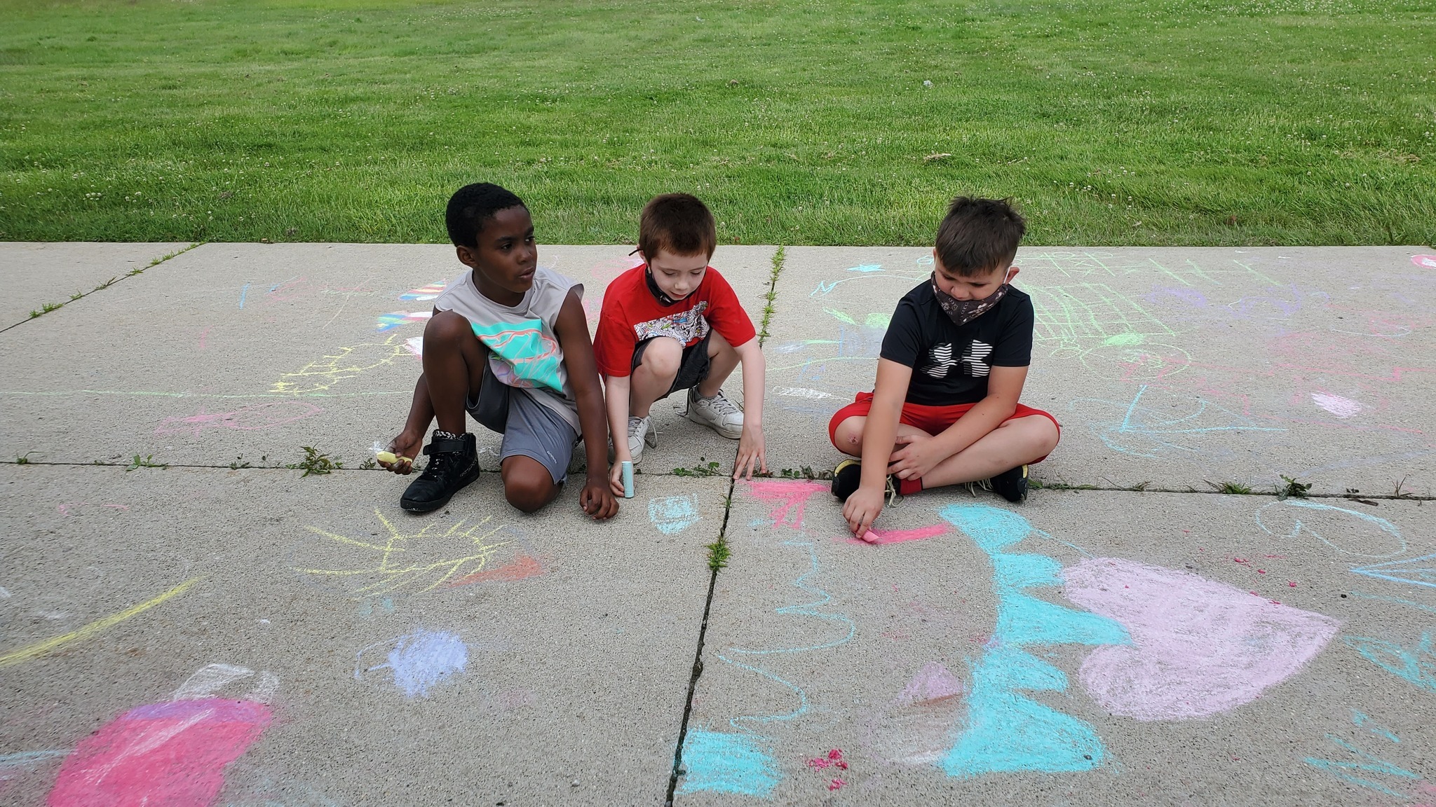 Three boys draw on pavement with sidewalk chalk