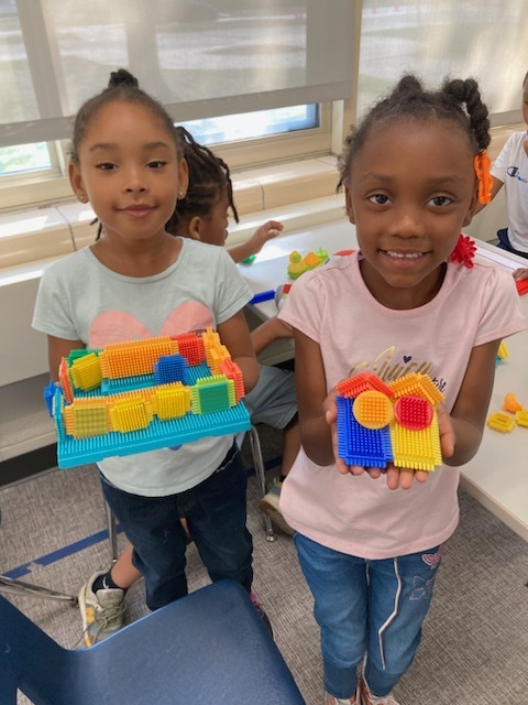 Two elementary girls holding up brick sculptures