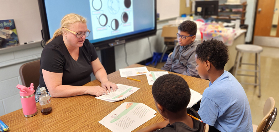 Summer program teacher works with three boys sitting at a table